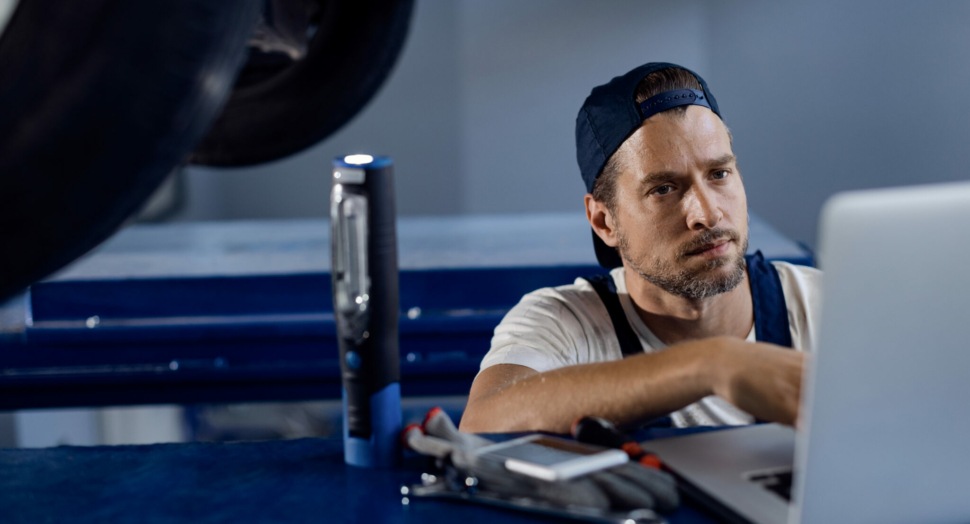 Auto repairman using computer while working in a workshop.